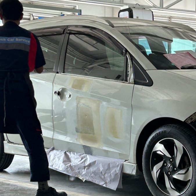 Teknisi memeriksa bagian depan kendaraan di area workshop